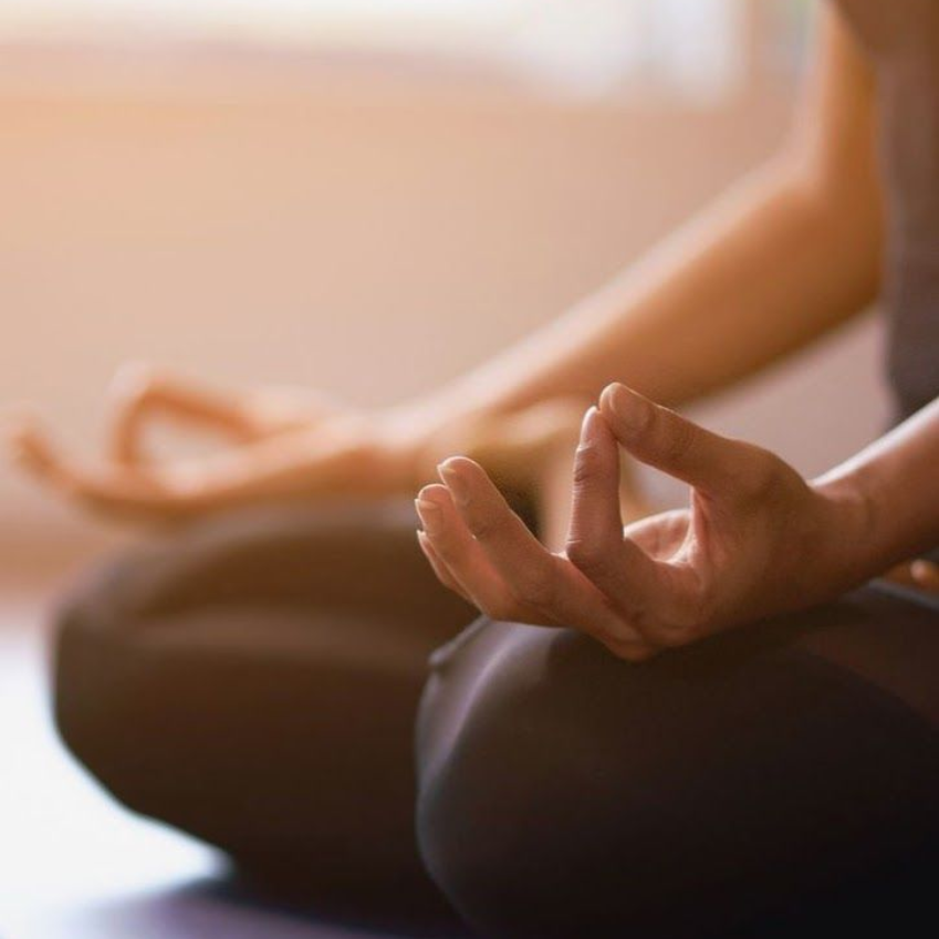 Een persoon zit binnenshuis met gekruiste benen en mediteert met zijn handen in een mudra-houding.