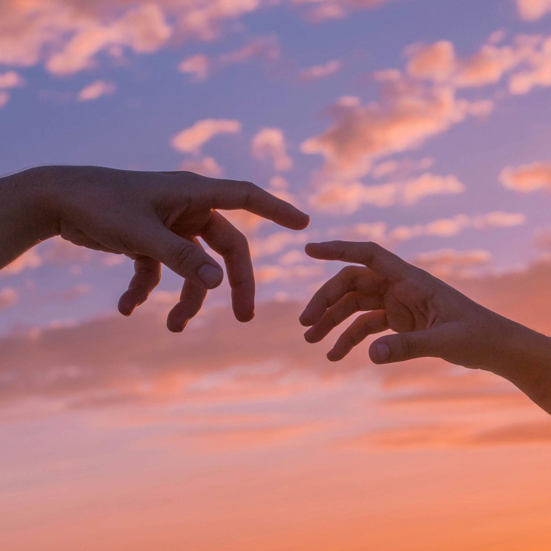 Twee handen die naar elkaar reiken tegen een roze en oranje zonsondergang.