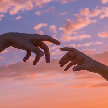 Twee handen die naar elkaar reiken tegen een roze en oranje zonsondergang.