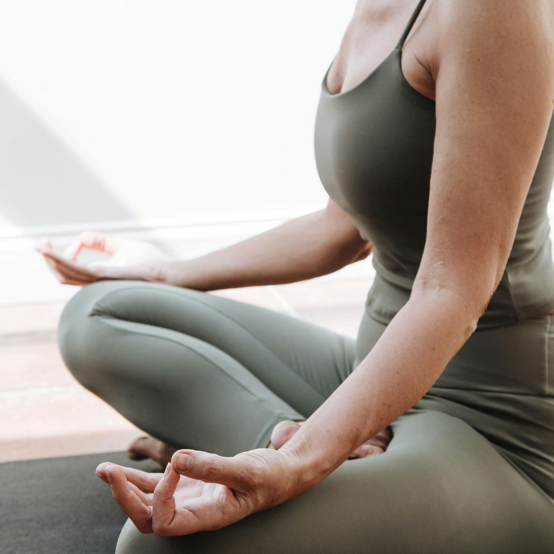 Vrouw in olijfgroene sportkleding mediteert in lotushouding.