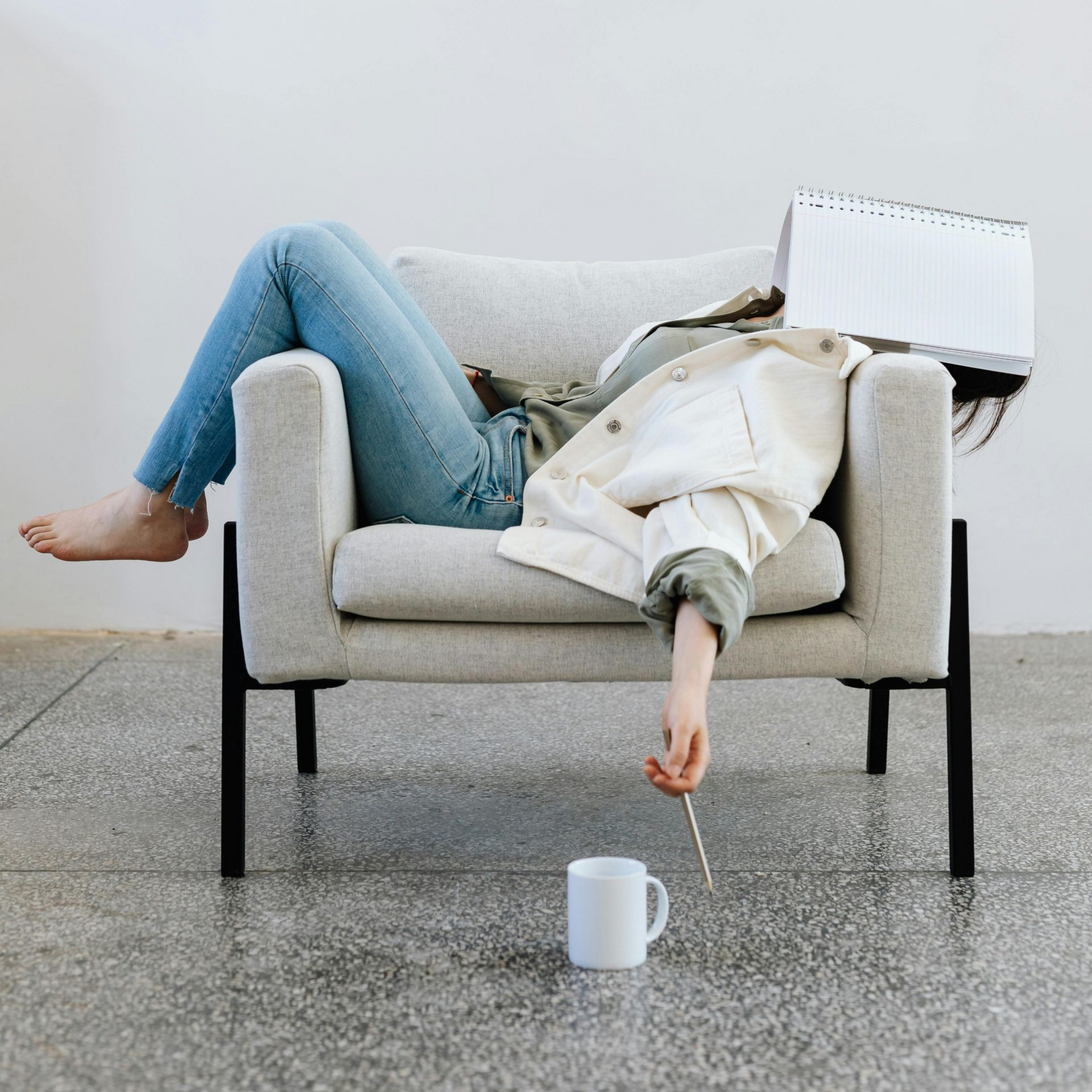 Persoon hangt onderuitgezakt in een fauteuil, zijn gezicht bedekt met een kalender, zijn arm bungelend naar een mok en een roerstaafje.