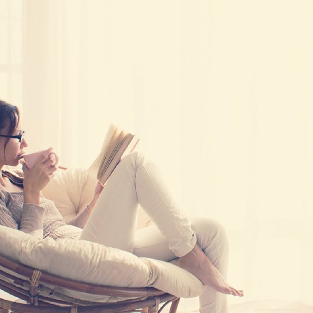 Een vrouw leest een boek en drinkt uit een roze mok in een comfortabele stoel.