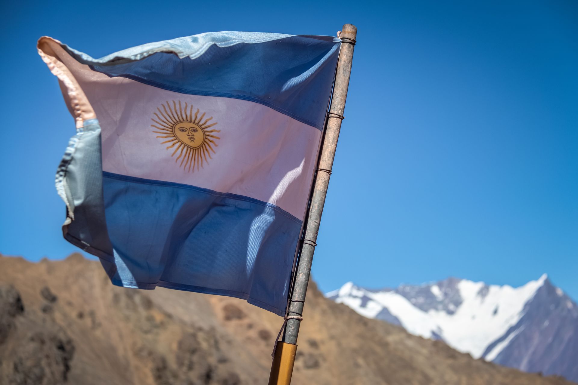 La bandera de Argentina ondea al viento con montañas de fondo.