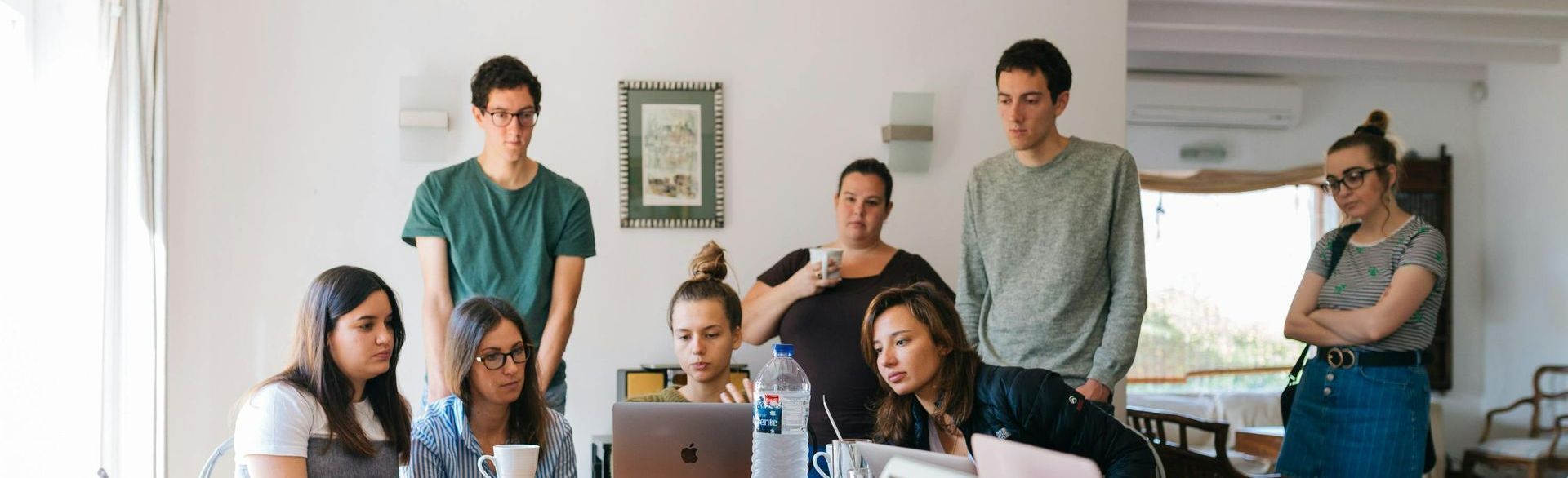 Um grupo de pessoas está sentado ao redor de uma mesa com um laptop.