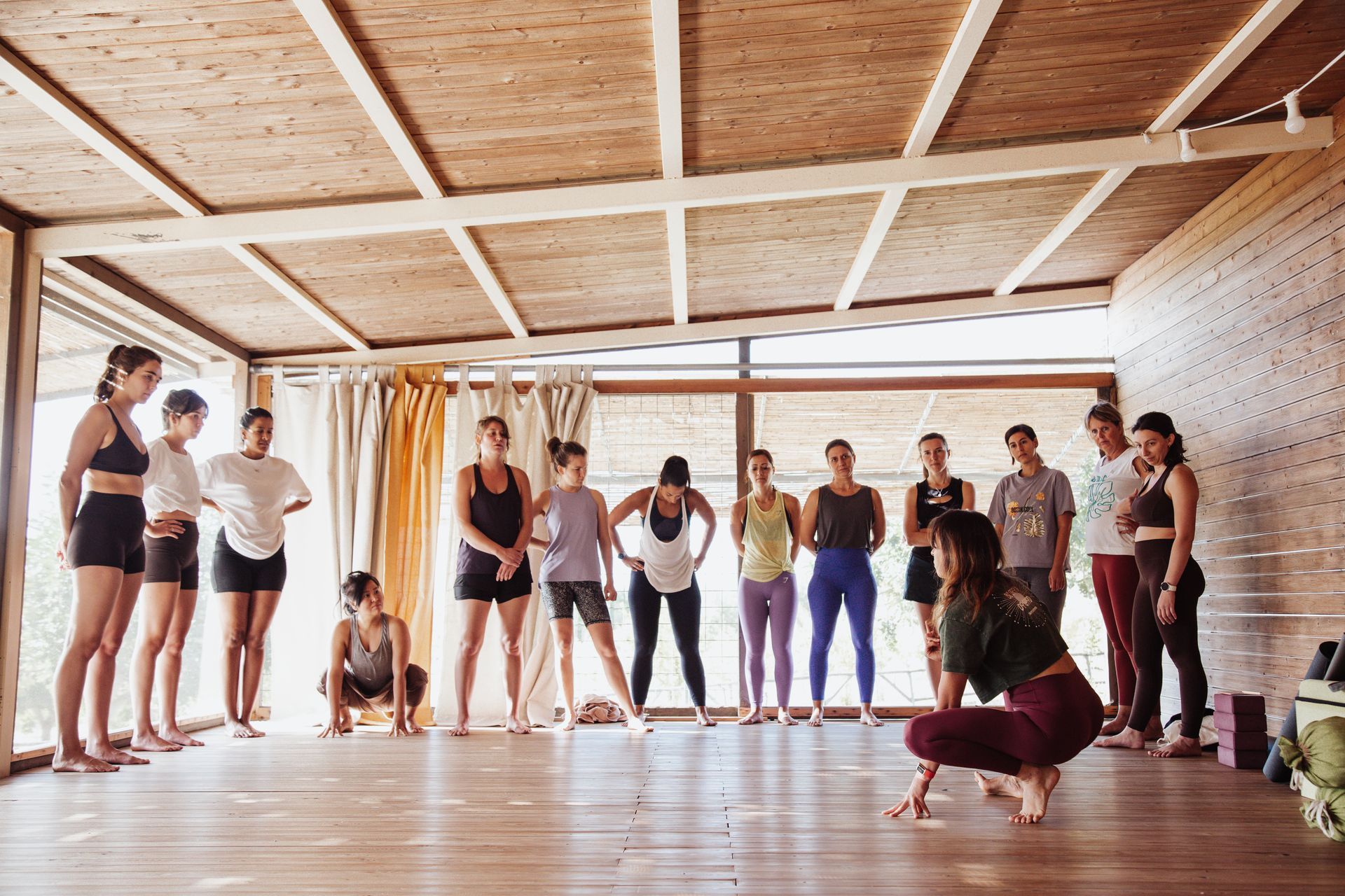 A yoga instructor demonstrates a pose to a group in a bright studio.