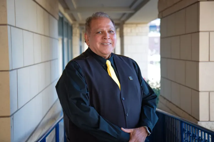 A man in a black vest and yellow tie is standing in a hallway.