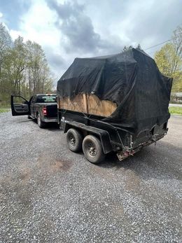 A pickup truck towing a trailer covered by a black tarp, parked on a gravel driveway.