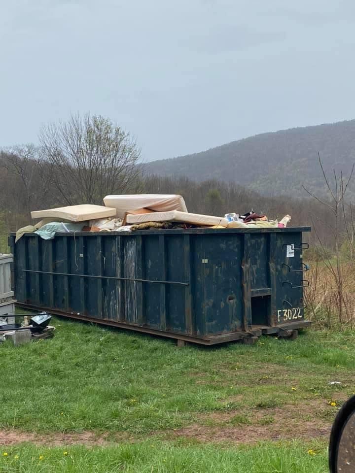 A dumpster filled with junk is sitting in a grassy field.