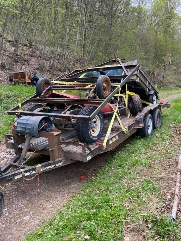 A trailer with a car on it is parked in a grassy field.