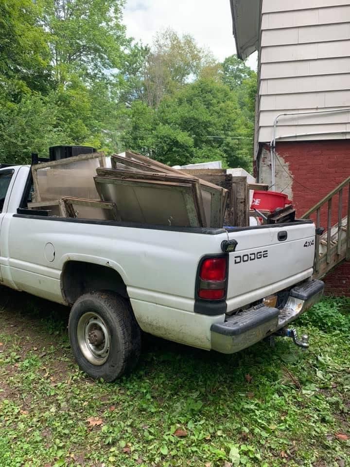 A white truck is parked in front of a house with wood in the bed.