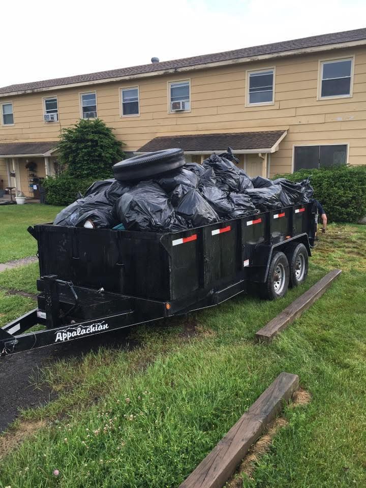 A dumpster trailer filled with trash bags is parked in front of a house.
