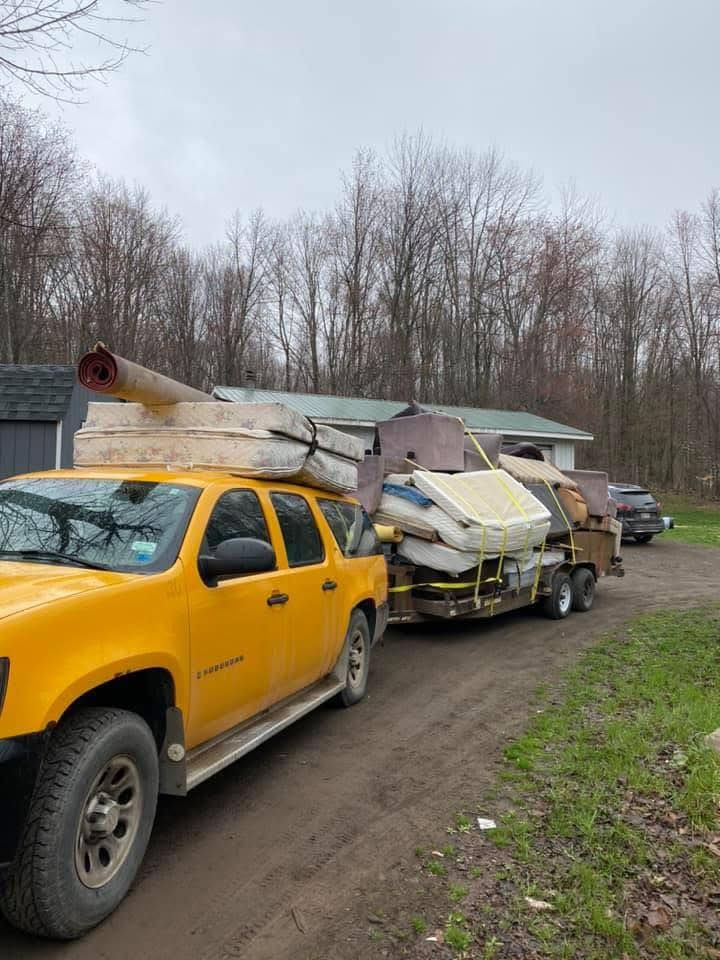 A yellow truck is pulling a trailer full of junk.