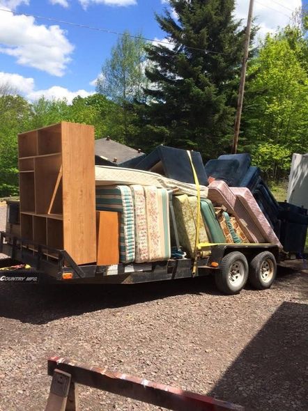 A trailer filled with furniture and mattresses is parked in a gravel lot.