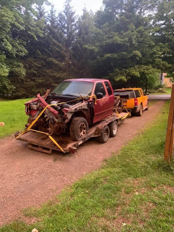 A red truck is being towed by a yellow truck on a trailer.