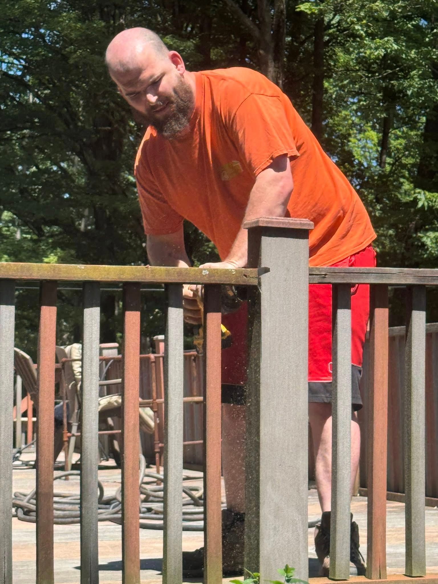 A man in an orange shirt is working on a fence