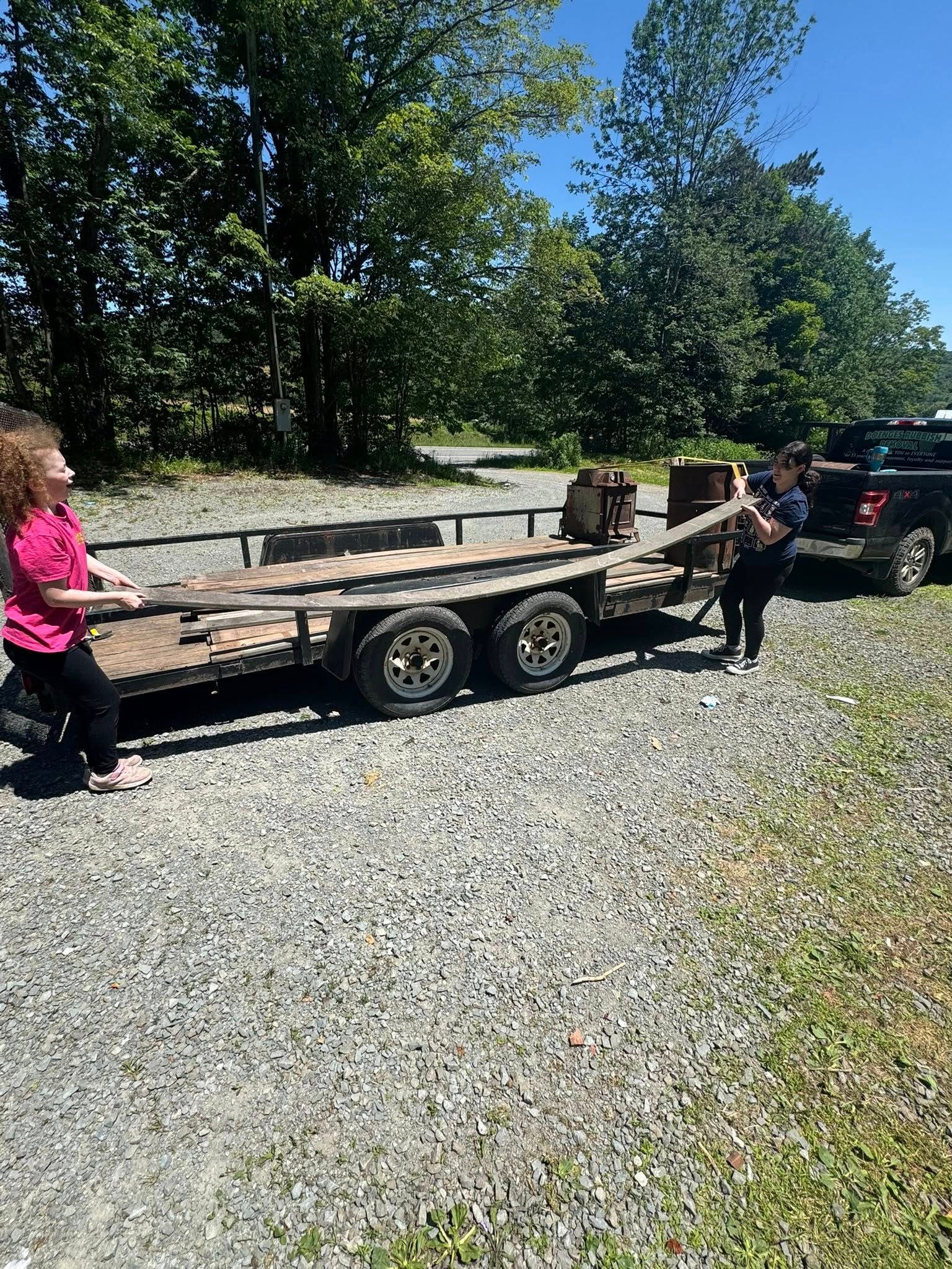 A couple of people are standing next to a trailer on a gravel road.