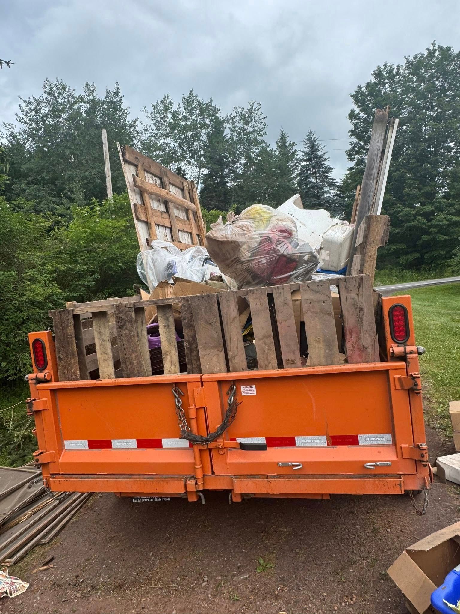 A dumpster filled with wooden pallets is parked on the side of the road.