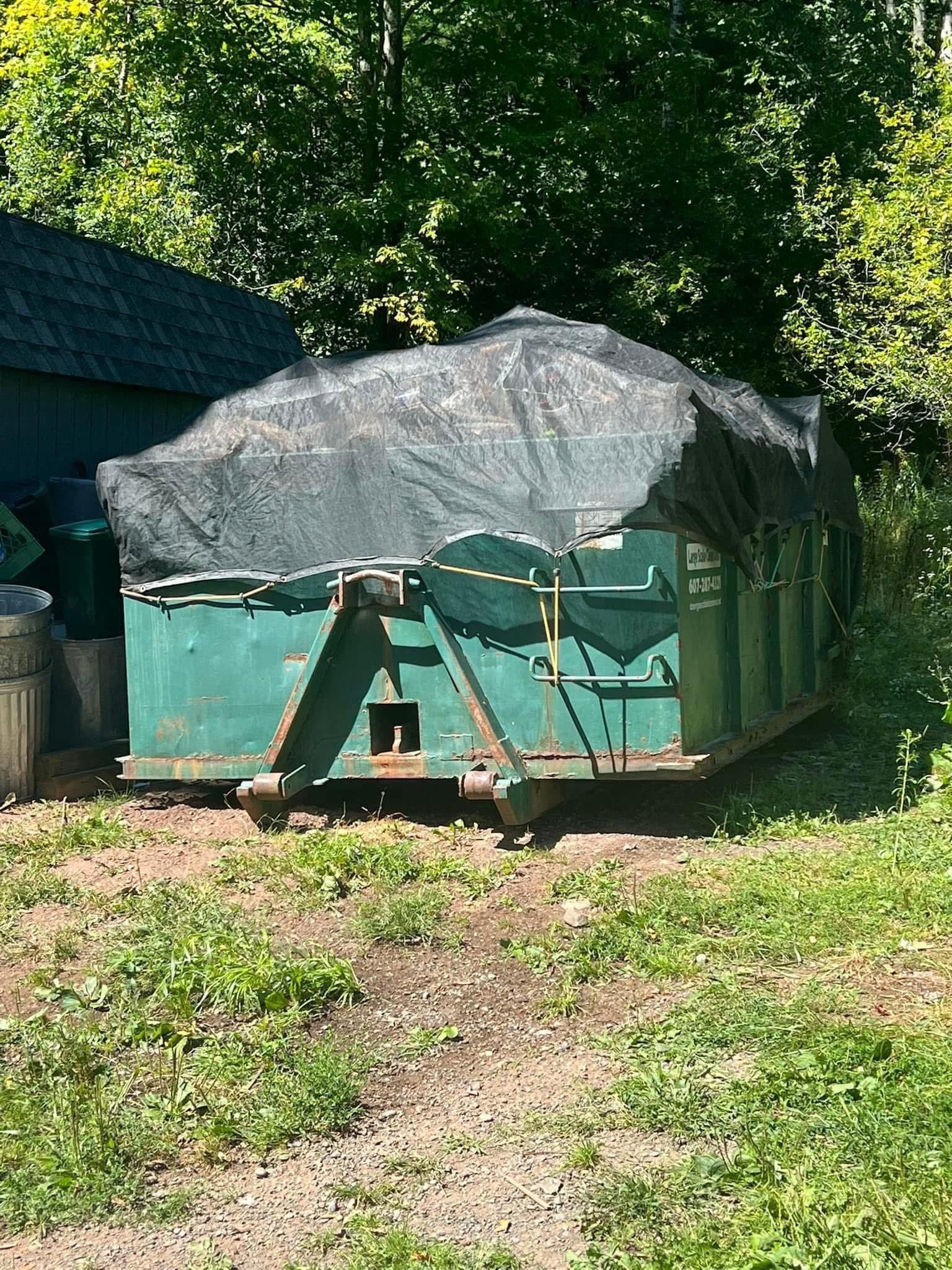 A green dumpster with a tarp on top of it is sitting in the grass.