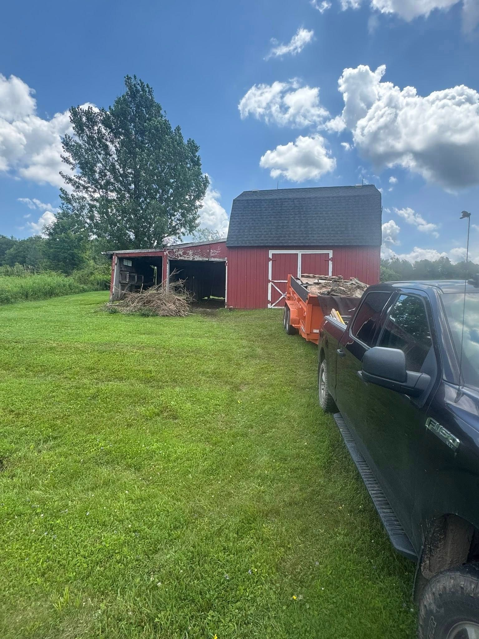 A black truck is parked in front of a red barn.