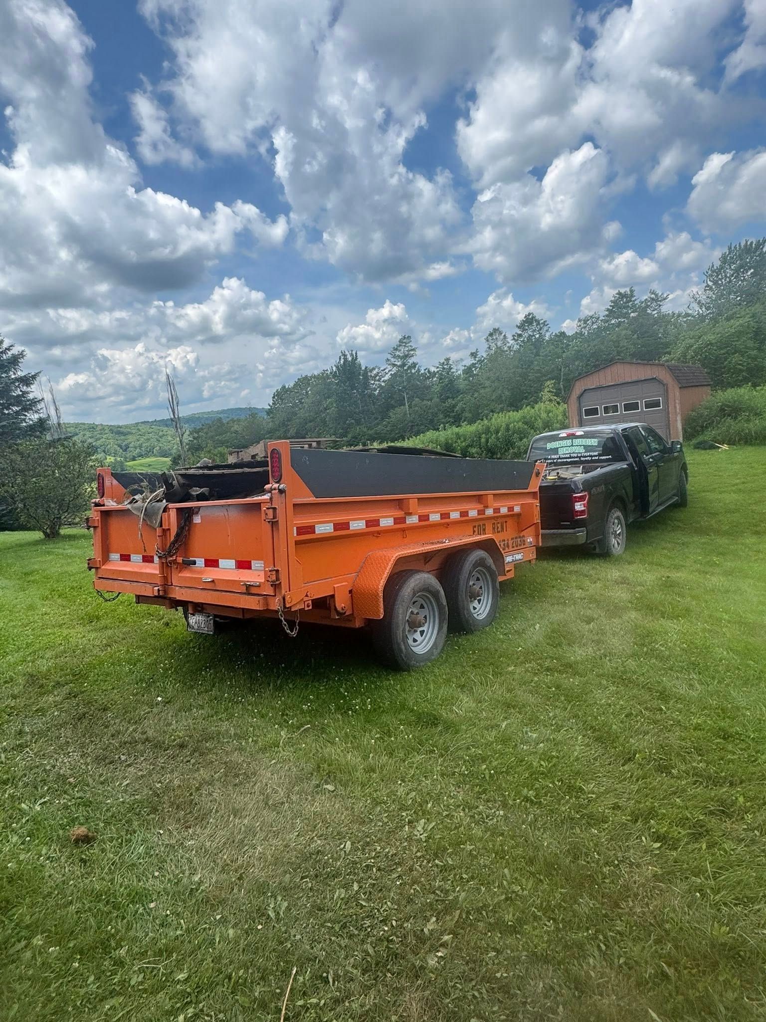 A dump trailer is parked in a grassy field next to a truck.