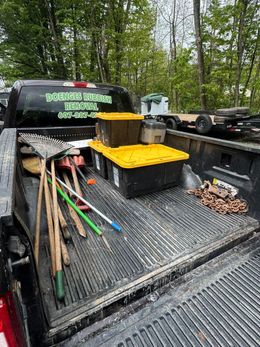 Pickup truck bed with tools, buckets, and branches in a wooded outdoor setting