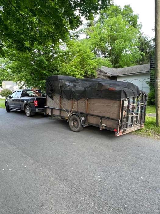 Red dumpster overflowing with trash in a wooded area; debris scattered around the base.