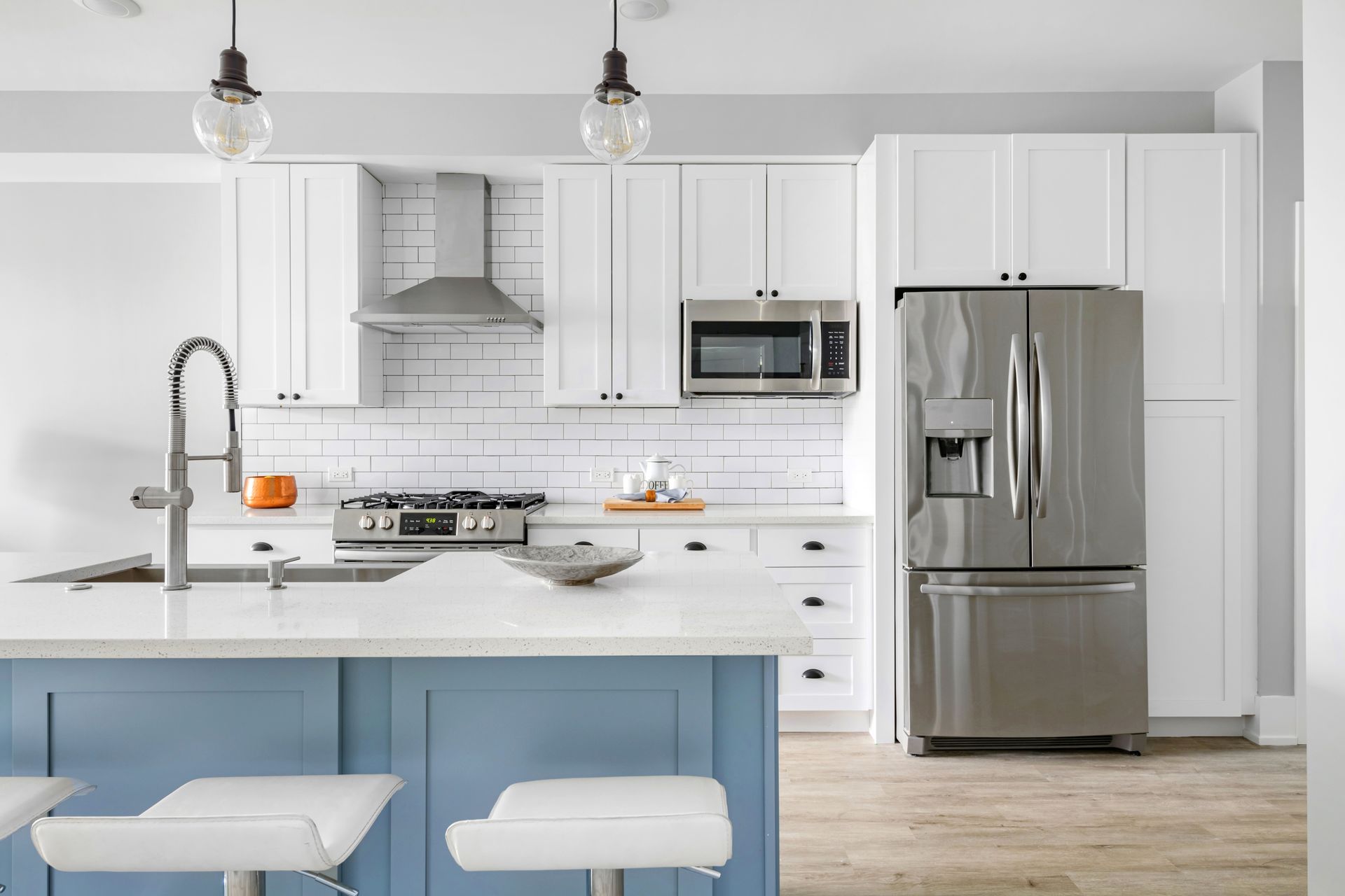 Modern kitchen with white cabinets, blue island, stainless steel appliances, and two pendant lights.