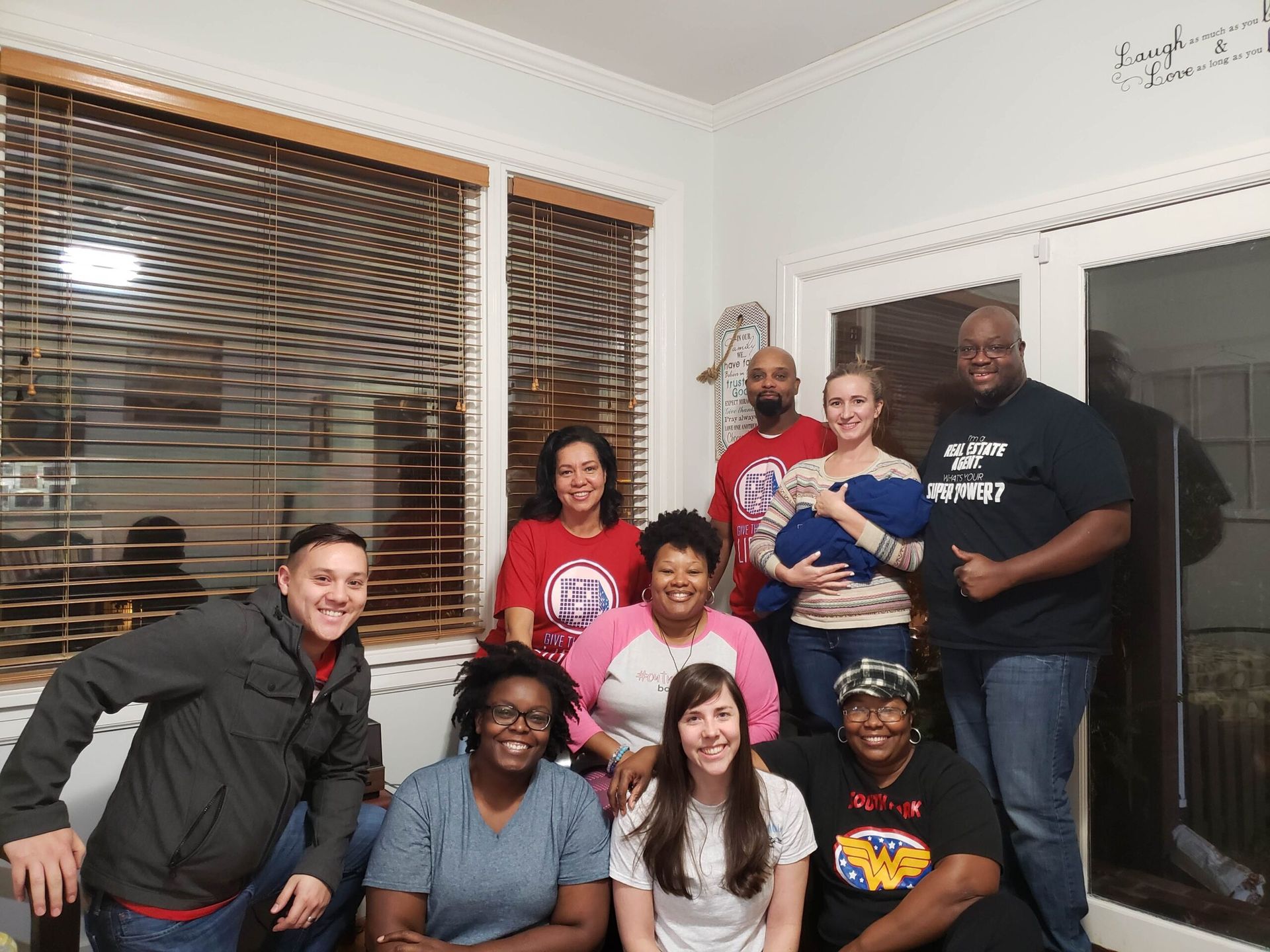 A group of ten people pose for a smiling portrait indoors, with some standing and others seated in front.