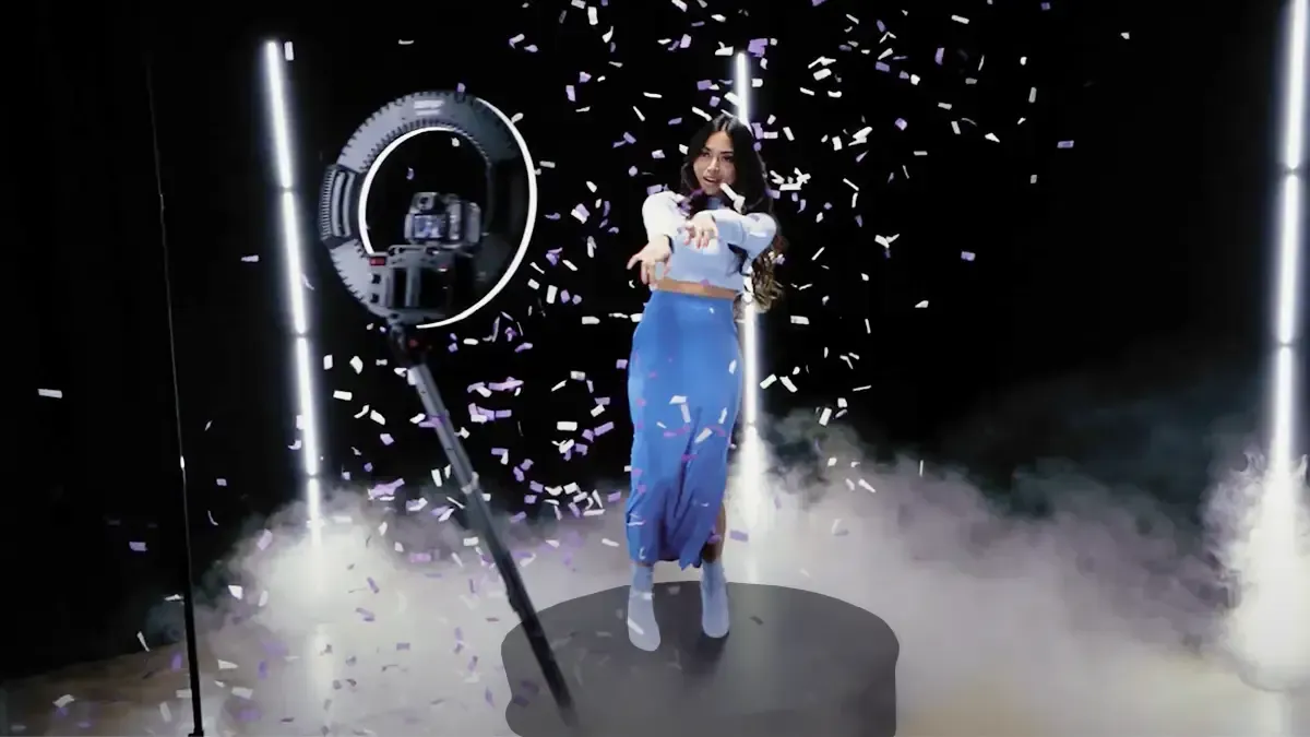 A woman in a blue dress is standing on a stage with confetti falling around her.