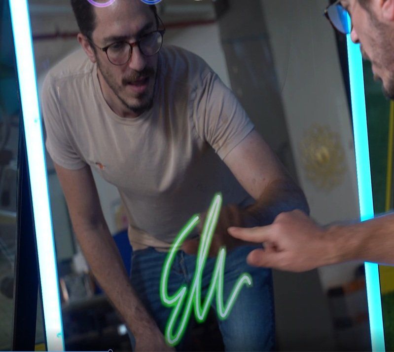 A man wearing glasses is looking at his reflection in a mirror