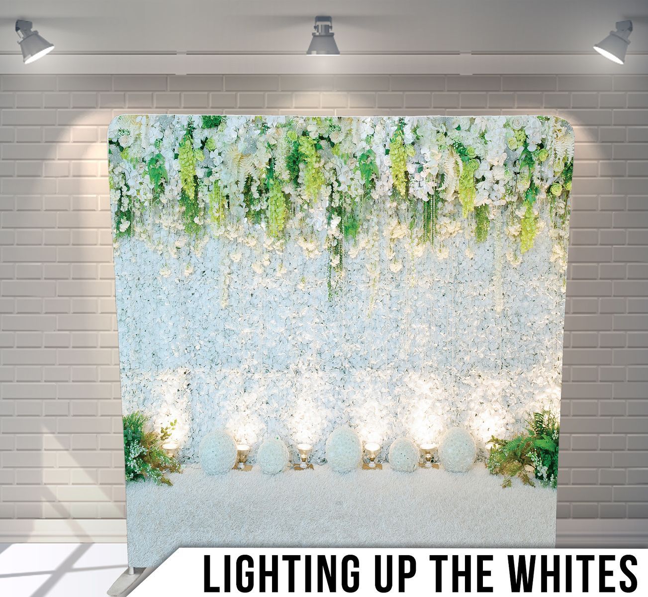 A wall with white flowers and green leaves is lit up with lights