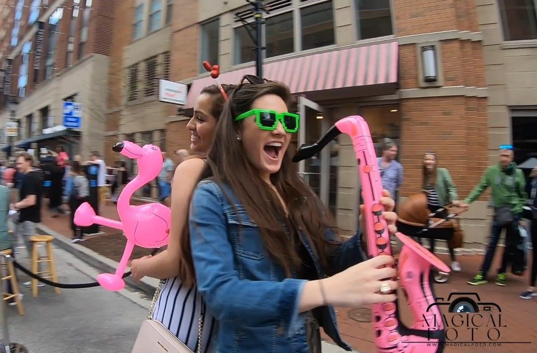 Two women are standing on a street with balloons on their heads.