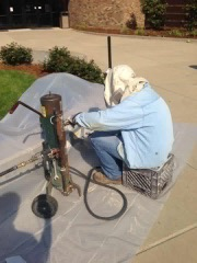 A man in a blue jacket is kneeling down and working on a machine.