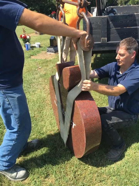 Two men are working on a large sculpture in a cemetery