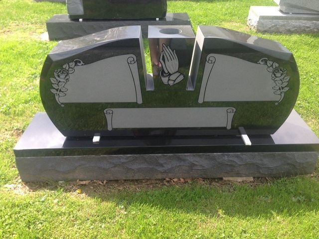 A black gravestone with praying hands on it is in a cemetery.