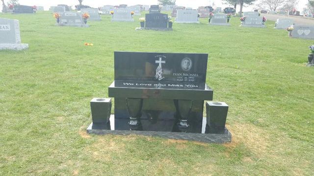 A black gravestone in a cemetery with a cross on it.