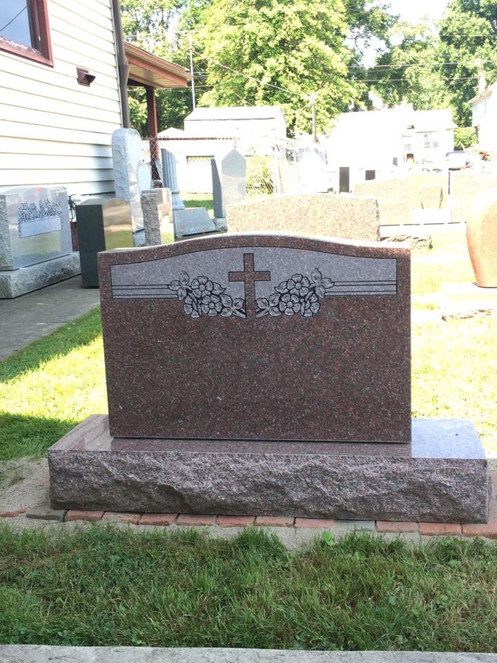 A gravestone with a cross on it is in a cemetery.