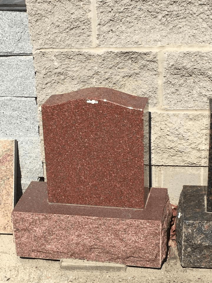 A red granite gravestone is sitting in front of a brick wall.