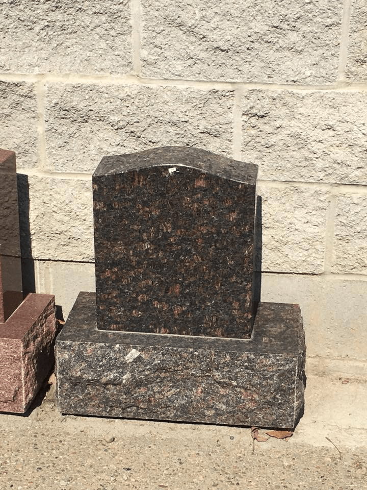 A gravestone is sitting in front of a brick wall.