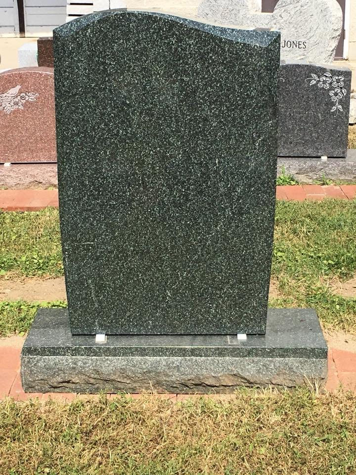 A green gravestone is sitting on top of a grass covered field.