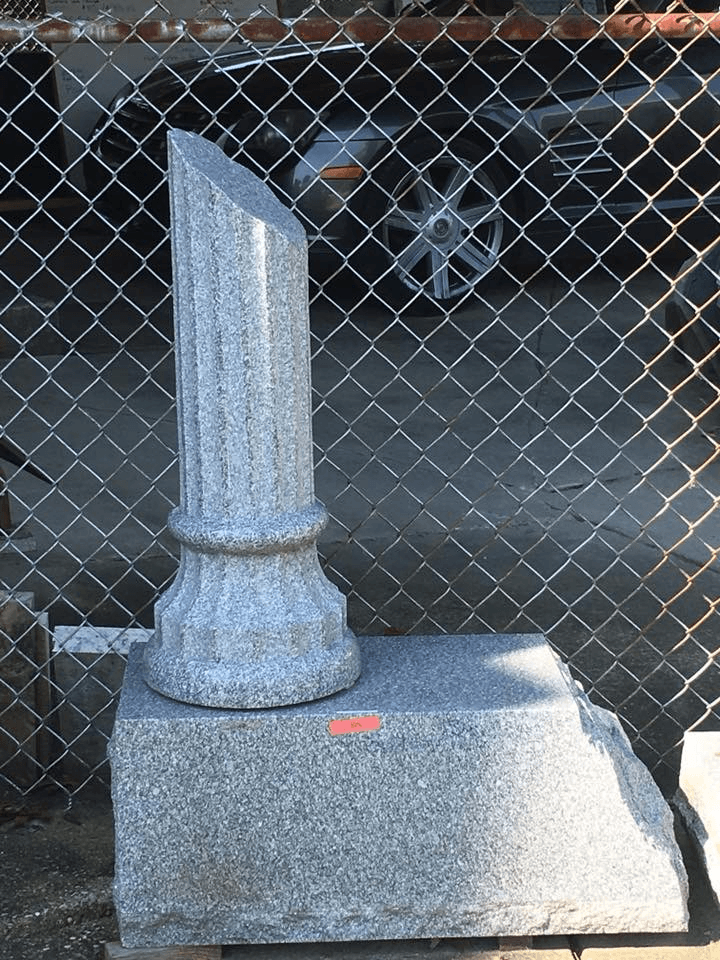 A gravestone with a broken column in front of a chain link fence