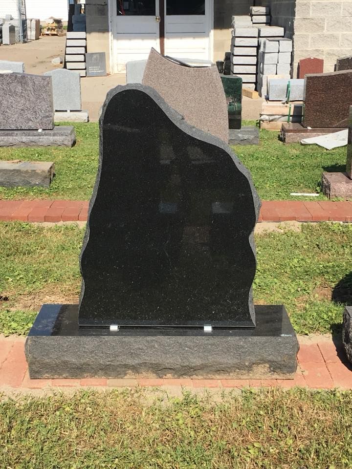 A black gravestone is sitting in the grass in front of a building
