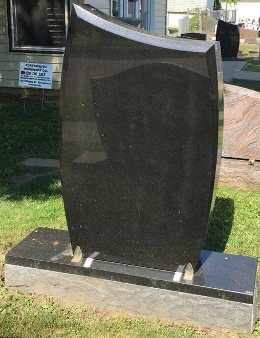 A black gravestone is sitting in the grass in front of a house.