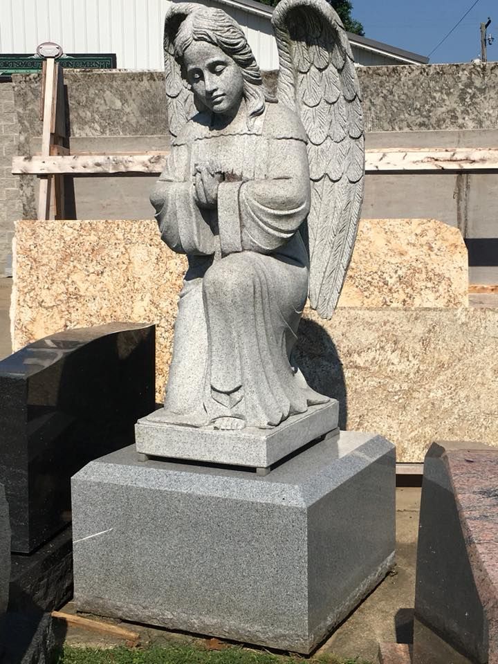 A statue of an angel is sitting on a pedestal in a cemetery.