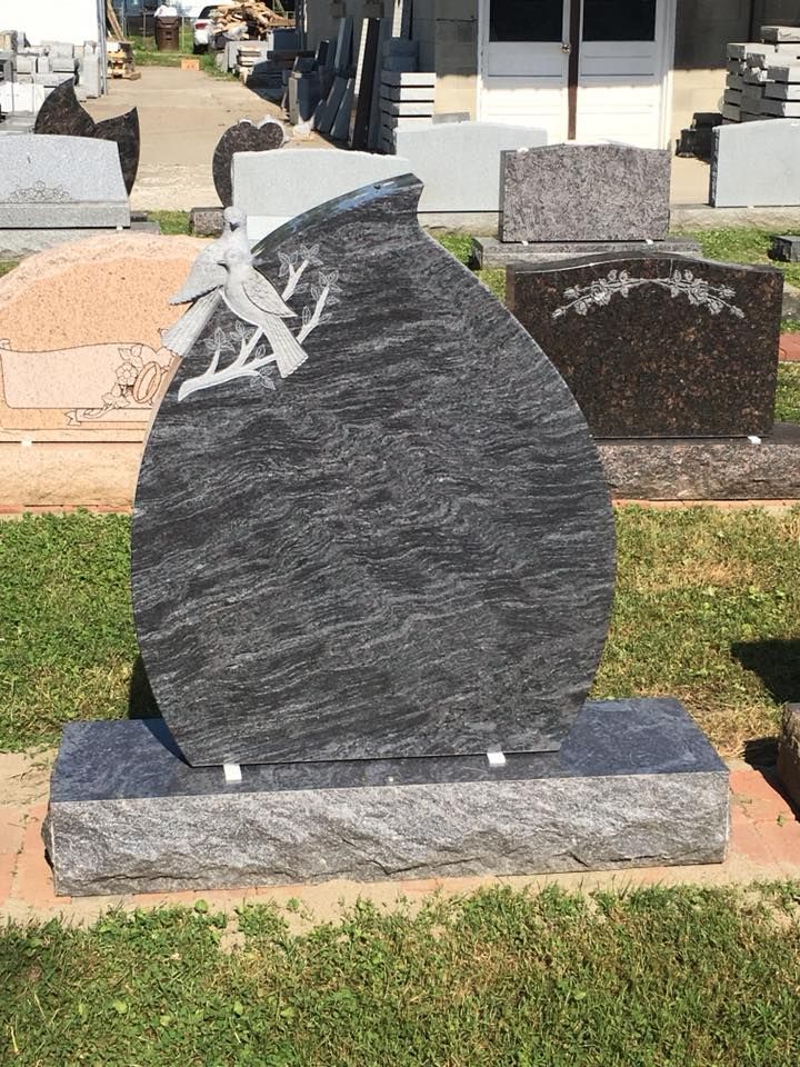 A gravestone with a bird on it is sitting in the grass in a cemetery.