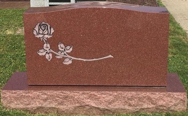 A red gravestone with a rose carved into it.