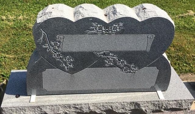 A gravestone in the shape of a heart is in a cemetery.