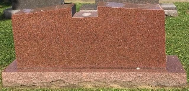 A red granite gravestone is sitting in the grass in a cemetery.