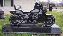 A gravestone in the shape of a motorcycle is sitting in the grass.