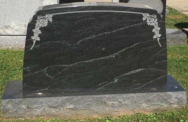 A black gravestone with roses on it is sitting in the grass.